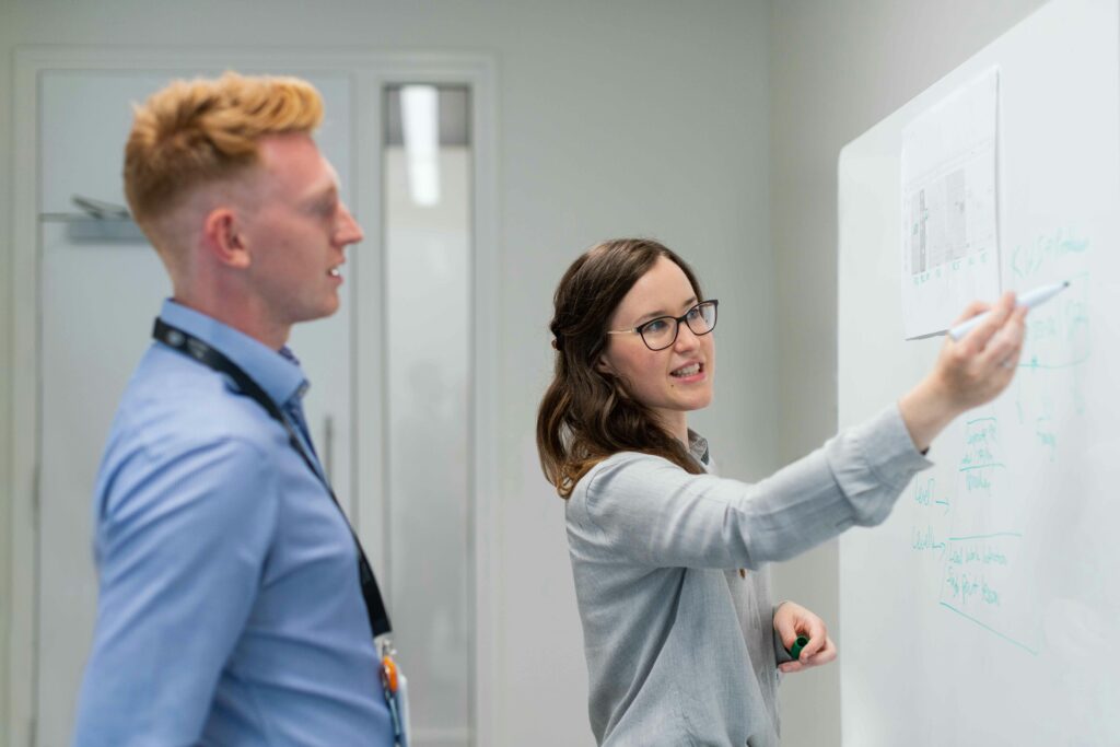 Two colleagues engaged in an office discussion at the whiteboard.