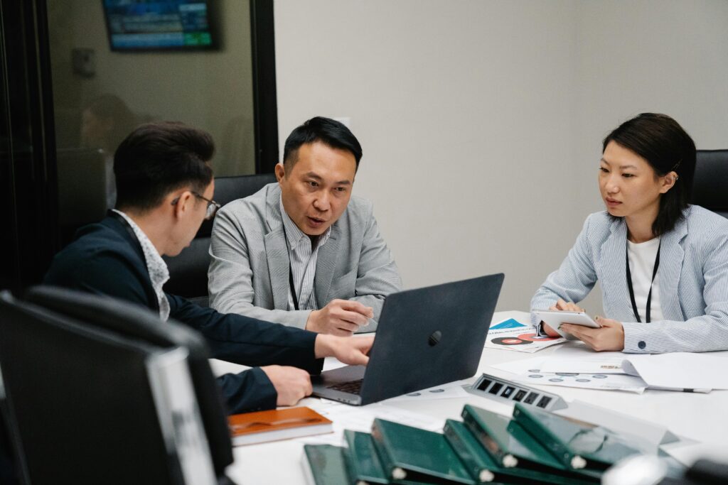 Three professionals engaged in a meeting, discussing strategies around a laptop in a modern office setting.